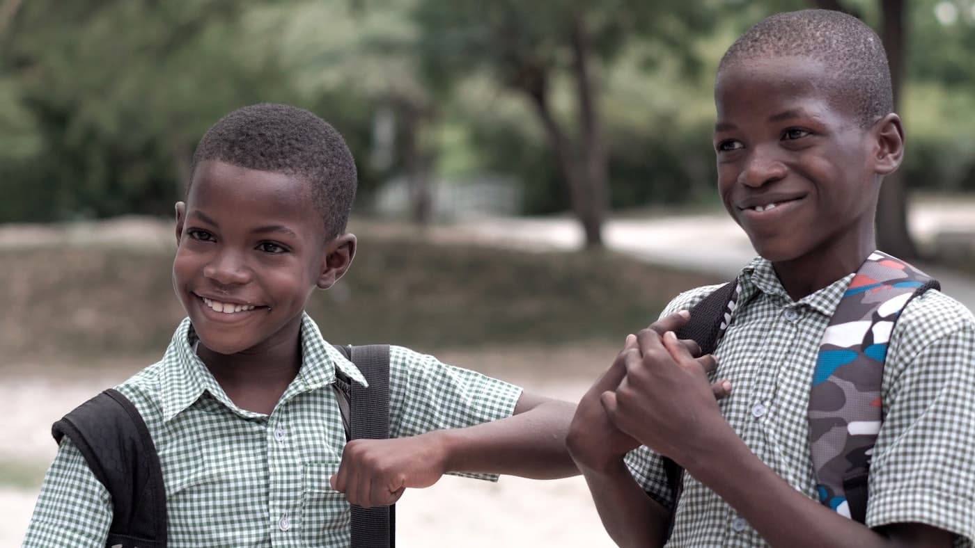 Deux écoliers en uniforme se saluent en souriant devant leur école